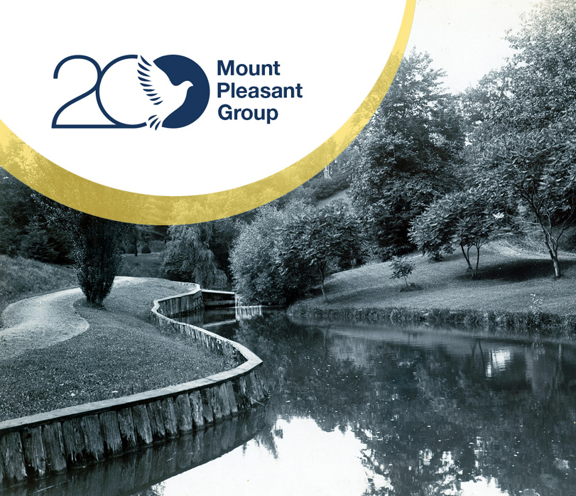 Mount Pleasant Group 20th‑anniversary logo overlaid on a vintage photograph of a winding creek surrounded by trees and landscaped greenery.