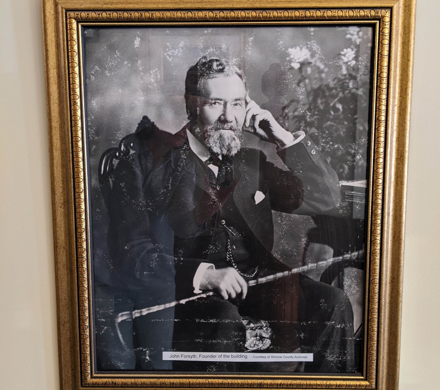 Black-and-white portrait of an older man seated, holding a cane, in a gold frame.