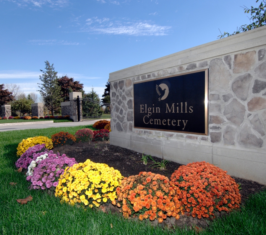 Exterior sign to Elgin Mills Cemetery with flowers at base