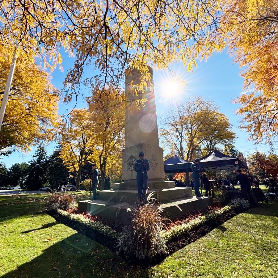Stone memorial with wreaths under autumn trees and sunlight.