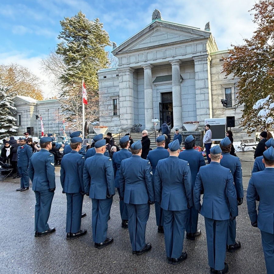 Uniformed personnel stand in formation facing a stone memorial building during an outdoor ceremony.