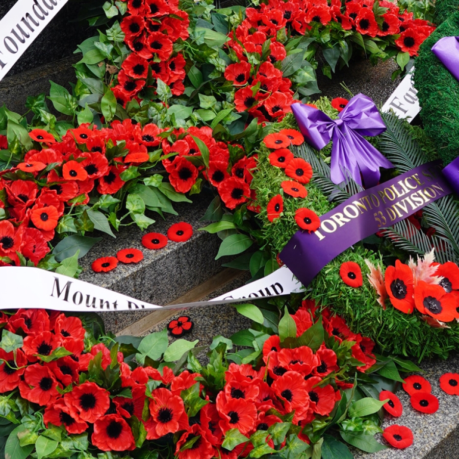 Close-up of memorial wreaths with red poppies and ribbons laid on a stone monument.