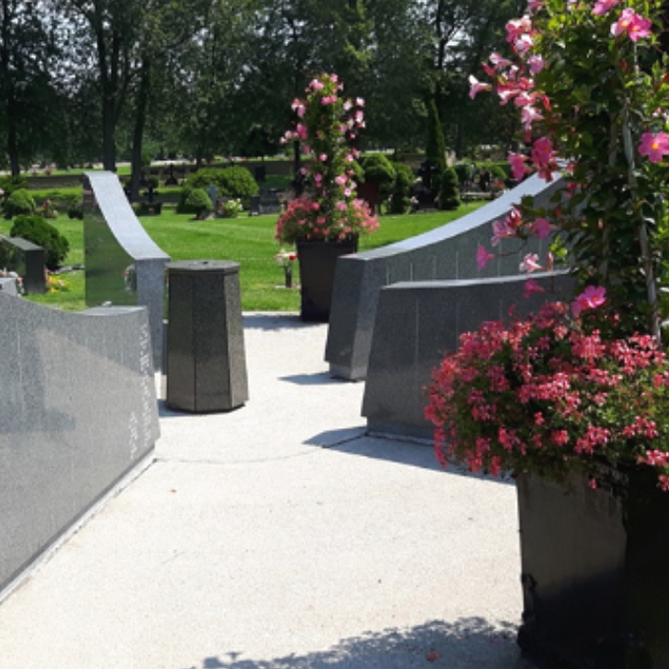 Pathway through a landscaped cemetery with curved stone memorials and flower planters.
