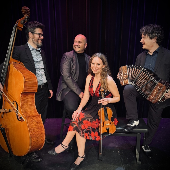 Four musicians on stage with double bass, violin, and accordion, posing together.
