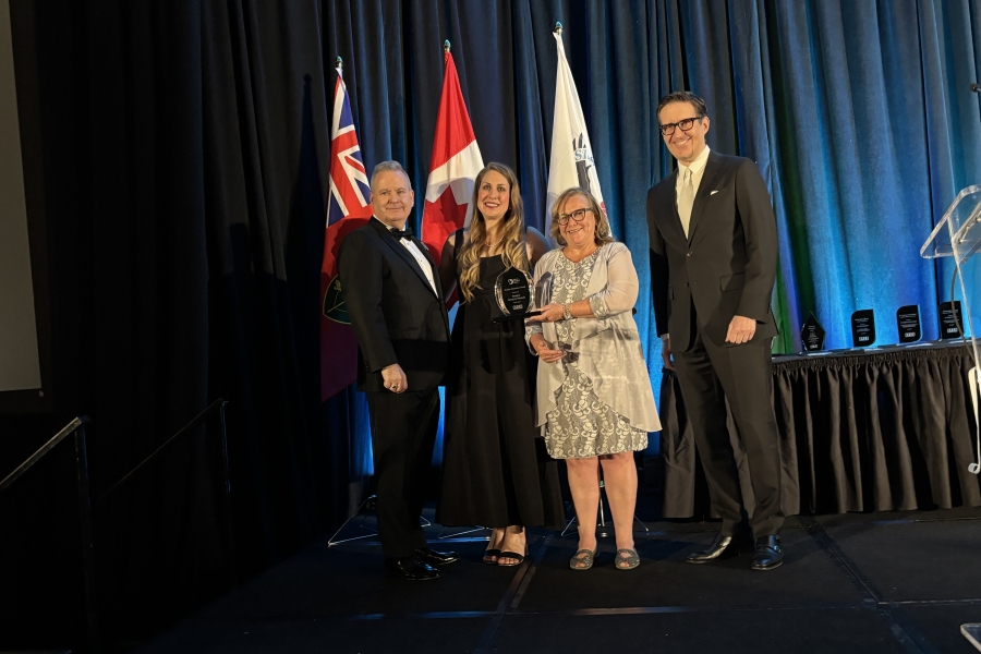 Four people in formal attire pose on stage as two women hold an award.