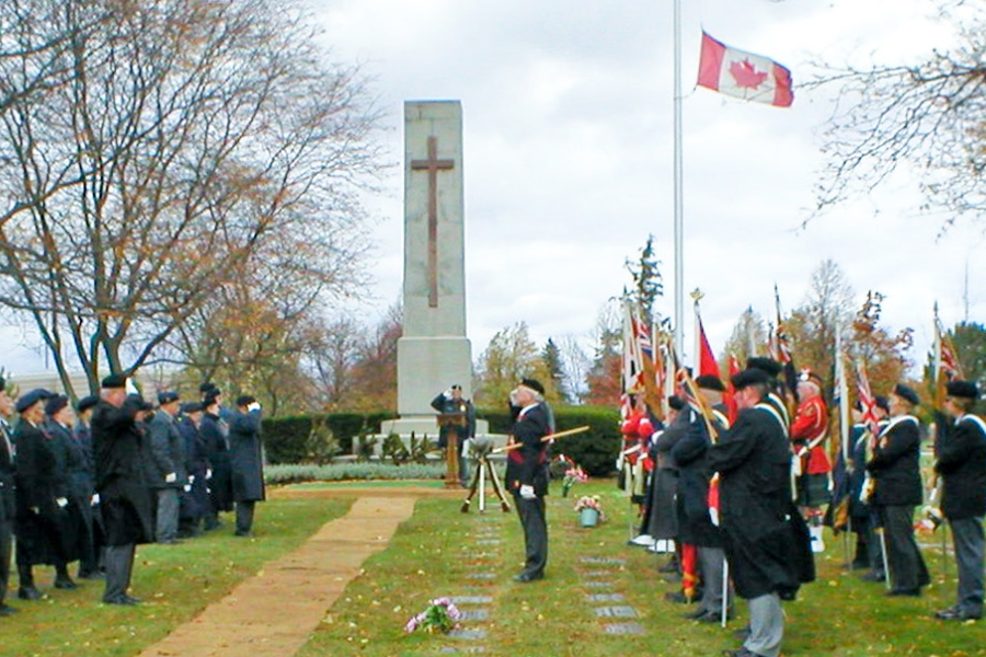 Remembrance Day ceremony at Beechwood with uniformed personnel, flag bearers, and a war memorial under autumn trees.