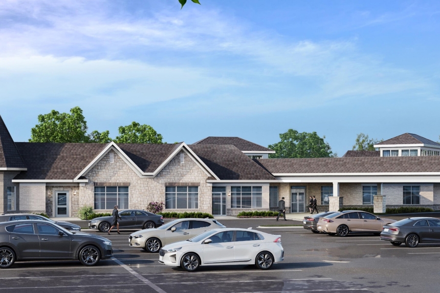Architectural rendering of a new funeral centre with a stone façade, covered entrance, landscaped grounds, and parking lot with several vehicles in front of the building.