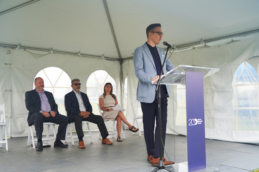 Speaker addressing attendees at a Mount Pleasant Group groundbreaking ceremony under an event tent.