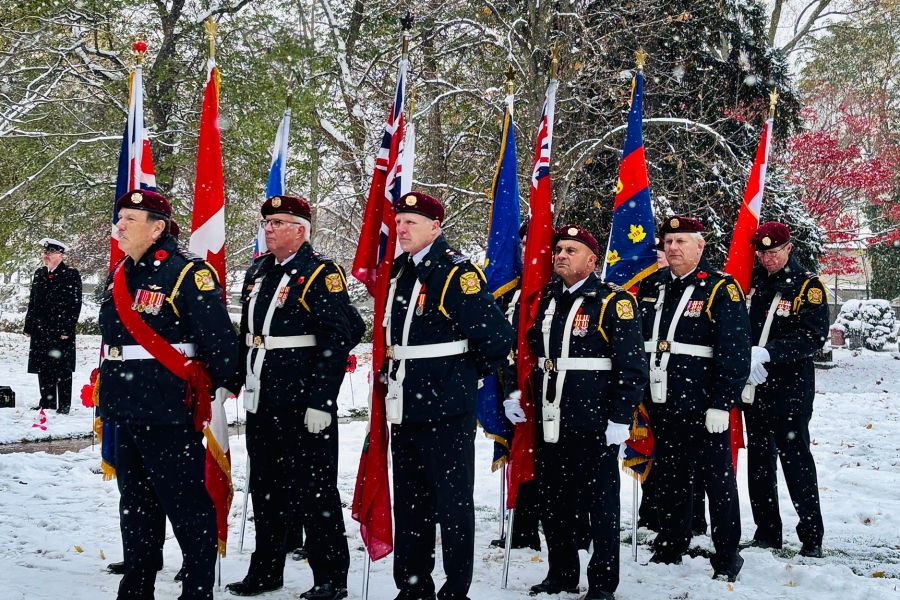 Honor guard members stand in formation outdoors in the snow, holding national and military flags.