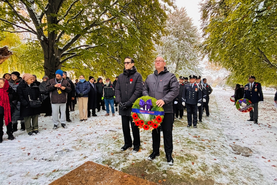 Two people holding a wreath with red poppies during a snowy remembrance ceremony, with others standing behind.