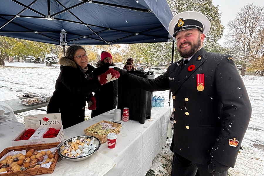 Man in military uniform receives a red poppy at outdoor winter remembrance event under a canopy.