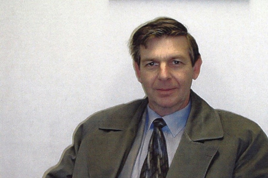 Person seated indoors wearing a coat and tie, holding a document.