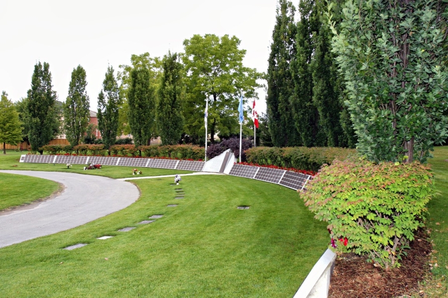 Curved path with memorial plaques and flags in a landscaped cemetery.