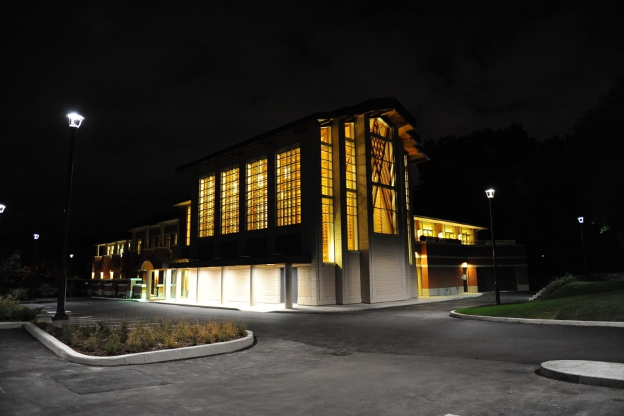 Contemporary building at night with tall lit windows and surrounding pathway and streetlights.