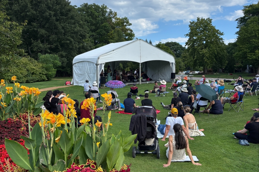 Outdoor event with audience seated on lawn facing a tented stage.