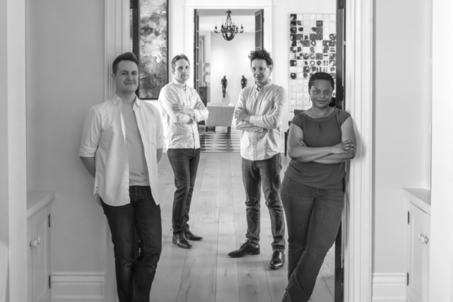Four musicians standing in a doorway and hallway, posing without instruments (black and white).