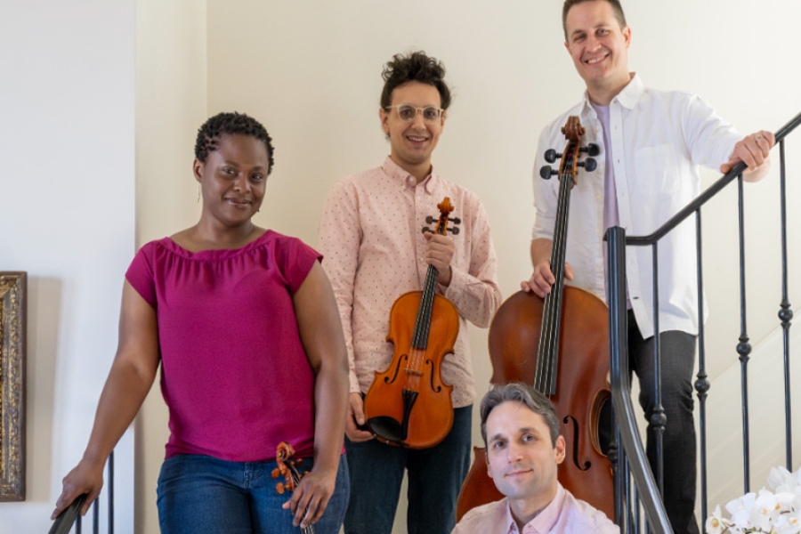 Four musicians holding violins and a cello, posed on a staircase.