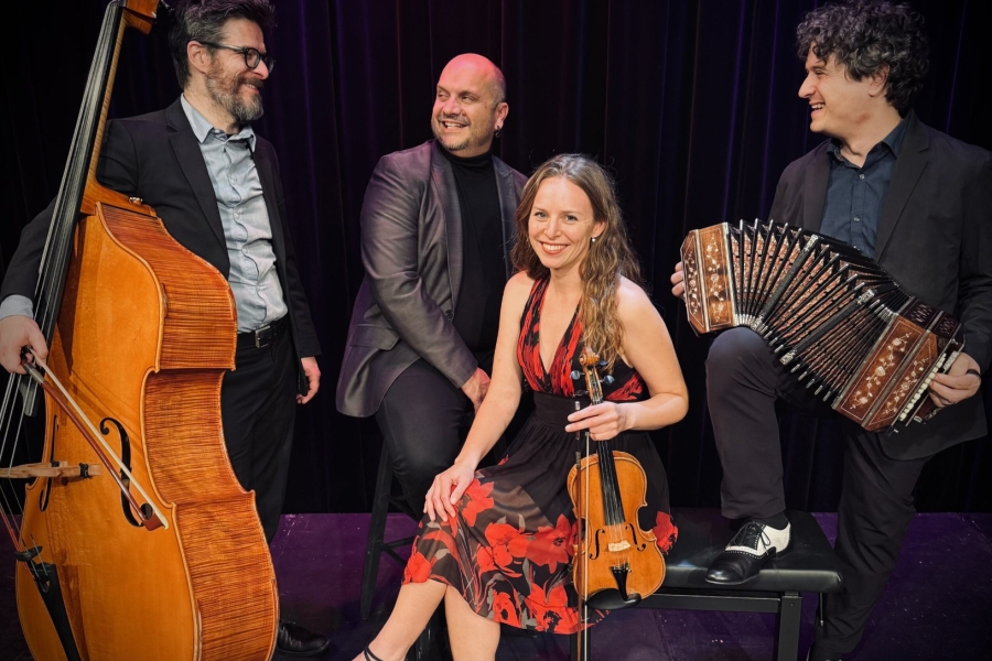 Four musicians on stage with double bass, violin, and accordion, posing together.