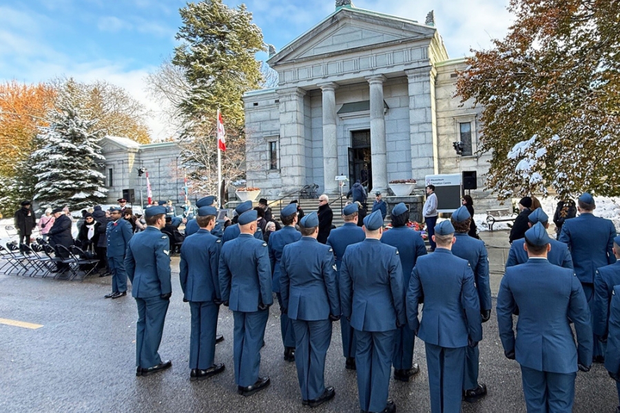 Uniformed personnel stand in formation facing a stone memorial building during an outdoor ceremony.
