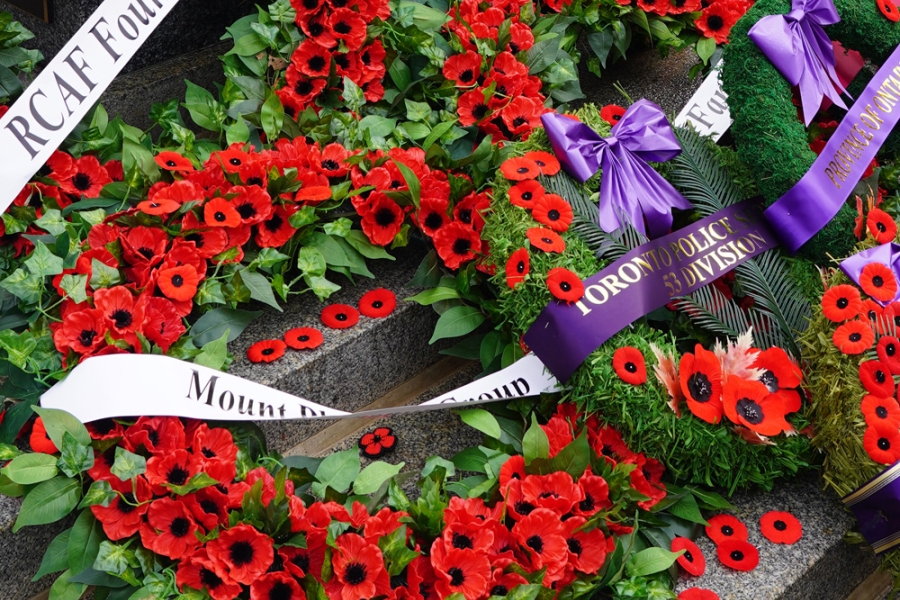 Close-up of memorial wreaths with red poppies and ribbons laid on a stone monument.
