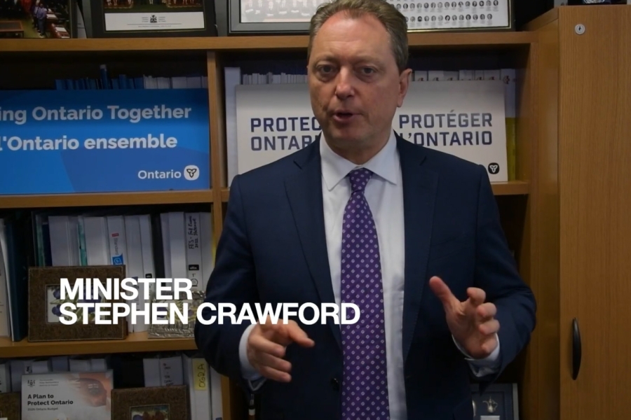 Minister Stephen Crawford speaking in an office, standing in front of shelves with Ontario signage and documents.