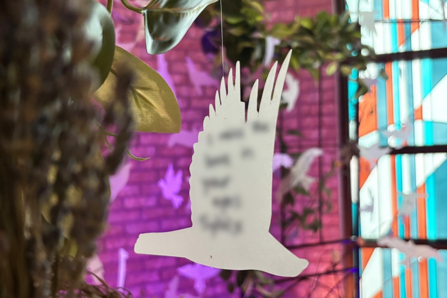 White bird-shaped ornament hanging among green leaves with colorful lighting in the background