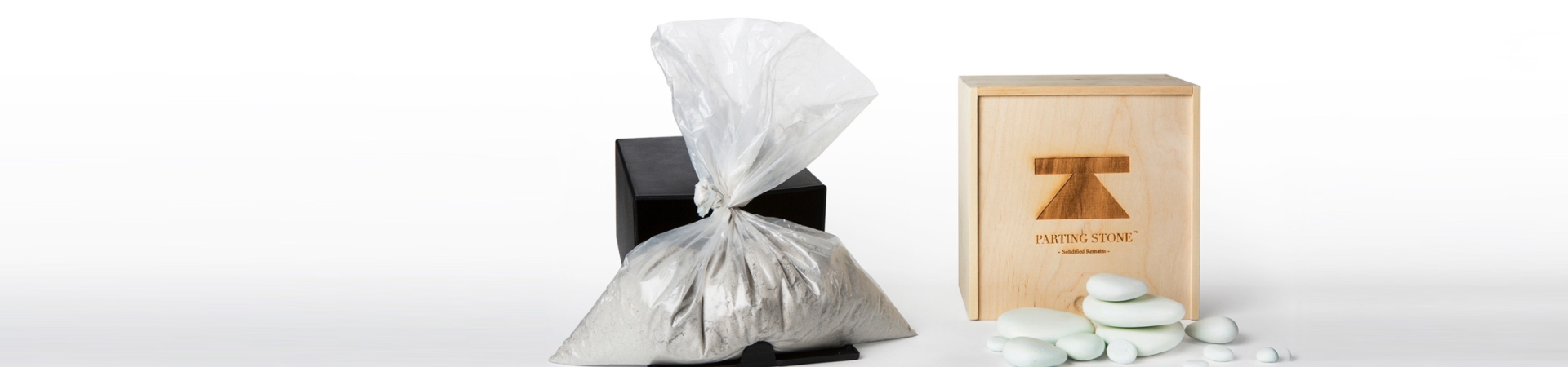 Bag of cremated remains with urn box and decorative stones on a white background.